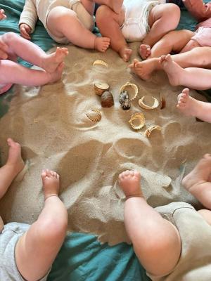 Im Sand mit Muscheln spielende Babys